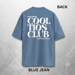 May include: Blue jean-colored t-shirt with the text "COOL TIOS CLUB" in large white letters on the back. The text "PROUD MEMBER" is above the club name, and "LIKE A DAD BUT COOLER" is below. The word "BACK" is at the top.