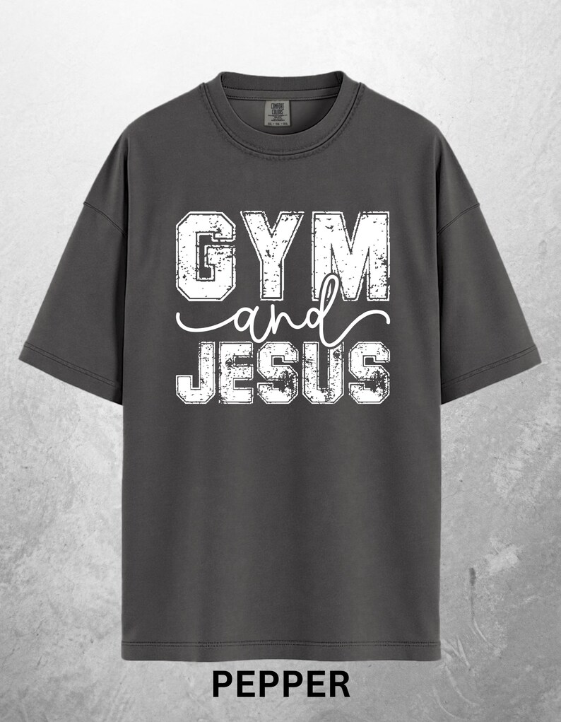 May include: A dark gray t-shirt with the words "GYM and JESUS" in distressed white lettering. The word "PEPPER" is printed in white at the bottom of the shirt. The shirt has short sleeves and a crew neck.