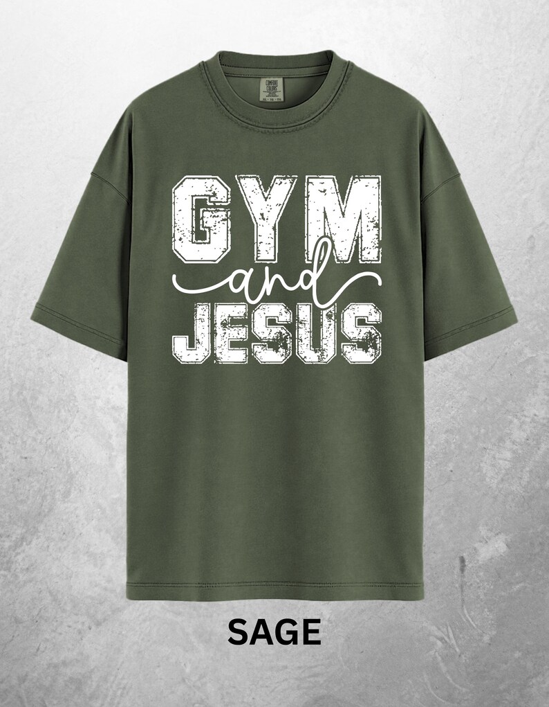 May include: Sage green t-shirt with the words "GYM and JESUS" in distressed white lettering. The shirt has a crew neck and short sleeves. The word "SAGE" is printed at the bottom of the shirt.