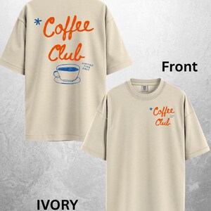 Może przedstawiać: Kremowe koszulki z napisem "Coffee Club" w pomarańczowym skrypcie z przodu i z tyłu. Z tyłu znajduje się niebieska grafika filiżanki do kawy oraz napis "Limited Time Only". Koszulki mają luźny kr&oacute;j.