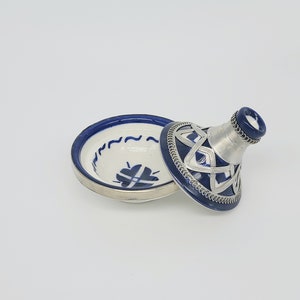 May include: A blue and white ceramic tagine with a silver trim. The tagine is open and the lid is sitting next to it.