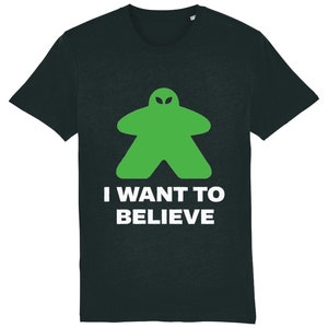 Peut inclure: T-shirt noir avec un pion de jeu en forme d'extraterrestre vert et le texte "I WANT TO BELIEVE" en blanc.