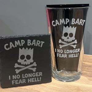 May include: A black pint glass and a black coaster with the words "CAMP BART" and "I NO LONGER FEAR HELL!" in white. The design includes a skull and crossbones with Bart Simpson's face. The glass is next to a square coaster.