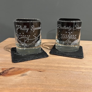 May include: Two clear glass shot glasses with black coasters. One glass has the text "Philly Special" etched on it and the other has the text "Brotherly Shove" etched on it. Both glasses feature a football play diagram.