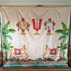 May include: A large fabric backdrop featuring a light beige background with a central red U-shaped tilak symbol flanked by a golden wheel and a white conch shell. Two white cows with red blankets stand on either side, framed by green banana trees.