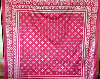 May include: A large, rectangular pink textile with a white geometric pattern and border. The design features a repeating floral motif and decorative edges, creating a symmetrical and ornate appearance. The textile is likely used as a decorative element.
