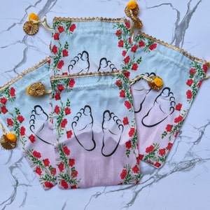 May include: Four light blue fabric drawstring bags with a floral pattern and baby footprints printed on them. The bags have yellow tassels.