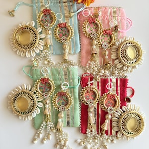 May include: An assortment of colorful, decorative pouches and ornaments. The pouches are in shades of blue, pink, green, and red, with gold accents. The ornaments feature floral designs, pearls, and tassels. A large, yellow-orange flower is in the background.