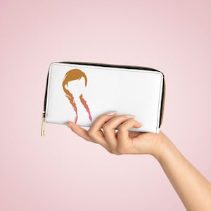 Puede incluir: Cartera blanca con cremallera con una silueta de una mujer con el pelo largo y trenzado en tonos naranja, rosa y rojo.