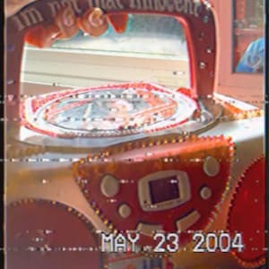 Pode incluir: Um brinquedo vermelho e branco com o texto "I'm not that innocent" na alça. O brinquedo tem uma tela e a data "MAY 23. 2004" é visível. O brinquedo é decorado com detalhes brancos e vermelhos.