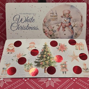 May include: A Christmas-themed box with a winter scene featuring a snowman and the text "I'm Dreaming of a White Christmas." The box contains a tray with festive illustrations and red foil circles.