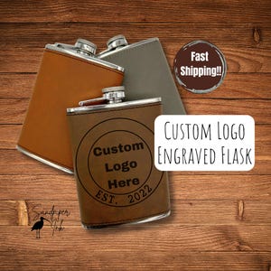 May include: Three leather-covered hip flasks in brown, grey, and tan, with silver tops. The front flask features a custom logo design with the text "Custom Logo Here EST. 2022" engraved. The text "CUSTOM LOGO ENGRAVED FLASK" is also visible.