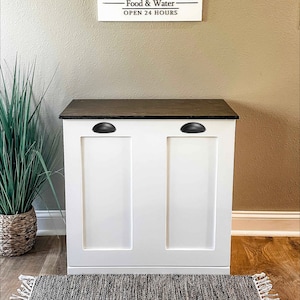 May include: White double-door cabinet with black knobs and a dark brown top. The cabinet has a sign above it that reads "Ernie's Doggy Diner - Food & Water - Open 24 Hours".