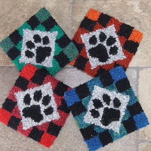 Pode incluir: Quatro tapetes quadrados, costurados &agrave; m&atilde;o, de cores vibrantes com um design de pegada de pata no centro. Os tapetes s&atilde;o feitos com uma variedade de cores, incluindo vermelho, preto, verde, azul e branco.