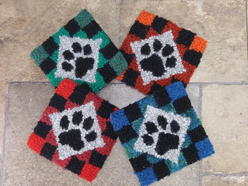 Pode incluir: Quatro tapetes quadrados, costurados &agrave; m&atilde;o, de cores vibrantes com um design de pegada de pata no centro. Os tapetes s&atilde;o feitos com uma variedade de cores, incluindo vermelho, preto, verde, azul e branco.