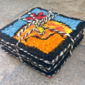May include: A set of six colorful woven coasters featuring a rooster design. The coasters are tied together with twine and have a black border.