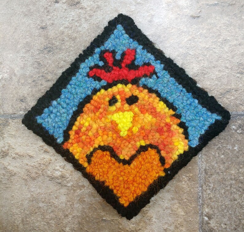May include: A colorful needlepoint design of a rooster with a red comb and a heart in its chest. The rooster is surrounded by a blue background with a black border.