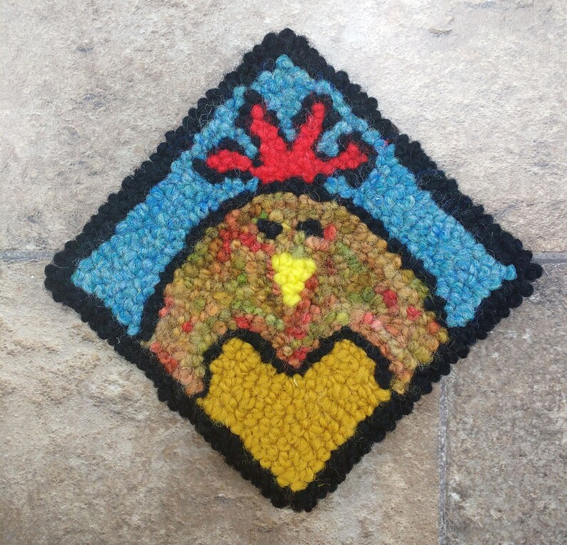 May include: A colorful wool rug depicting a rooster with a red comb and a yellow beak. The rooster is surrounded by a blue and black border.