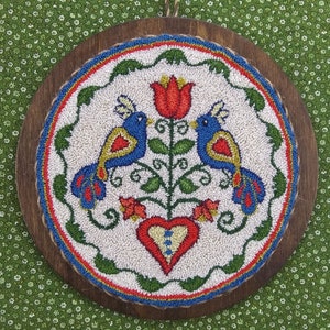 Puede incluir: Un tapiz de pared de punto de aguja enmarcado en madera con fondo blanco y un diseño colorido de dos pájaros azules, una flor roja y un corazón rojo.