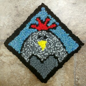 May include: A diamond-shaped rug with a black border and a gray, white, and yellow heart in the center. The heart is surrounded by a blue and red design.