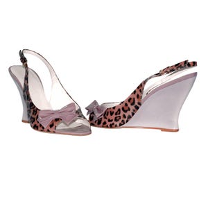 Op de afbeelding: Een paar lichtpaarse en bruine sandalen met wigvormige hakken, een luipaardprint en een strik op de teen.