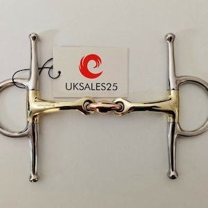 May include: A two-piece horse bit with a gold and silver finish. The bit has a loose ring on one side and a fixed ring on the other. The bit is labelled "UKSALES25".