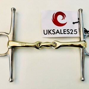 Pode incluir: Um freio de cavalo dourado e prateado com um anel solto em uma extremidade e um anel fixo na outra. O freio tem 14 cm de comprimento e tem a inscrição "UKSALES25" gravada.
