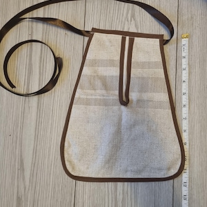 May include: A beige and brown striped fabric pouch with a brown ribbon strap and brown trim. A white measuring tape is placed alongside the pouch, showing a length of approximately 28 cm from the top edge to the bottom of the pouch.