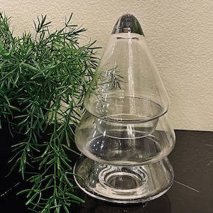 Puede incluir: Un portavelas de vidrio transparente con forma de árbol de Navidad de tres niveles. El portavelas está vacío y tiene un acabado liso y pulido.