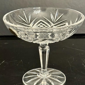 Op de afbeelding: Een helder dessertglas met steel. De kom heeft een breed, ondiep ontwerp met een decoratief sterrenpatroon. De steel is facetgeslepen en de voet is rond met een bijpassend sterrenpatroon. Het glas heeft een geslepen kristal uiterlijk.