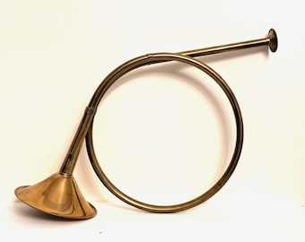 May include: A brass hunting horn with a flared bell and a circular design. The horn is a warm gold colour and is set against a white background. The horn is a musical instrument.