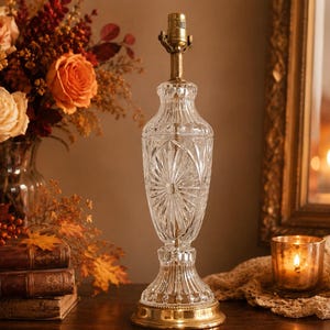 May include: A clear glass table lamp base featuring a vertical ribbed design and a starburst pattern on the body. The lamp has a brass-coloured metal base and a brass-coloured metal socket at the top, standing upright on a flat surface.