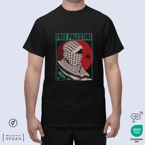 Pode incluir: Camiseta preta com um gráfico que diz "FREE PALESTINE". O gráfico apresenta uma pessoa usando um keffiyeh, um círculo vermelho e uma estrela. O design é emoldurado em verde.