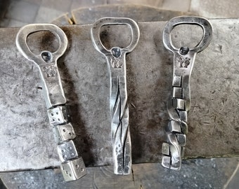 May include: Three metal bottle openers with different designs. The first opener has a dice pattern, the second has a twisted design, and the third has a chain link design.