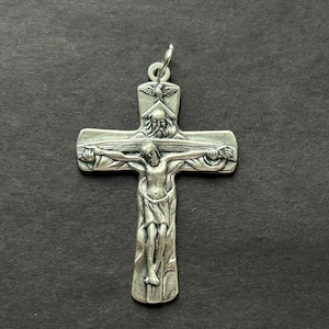 May include: Silver crucifix pendant with a detailed depiction of Jesus Christ. The cross features intricate carvings, including figures at the top and along the arms. It has a loop for hanging. The pendant is made of silver.