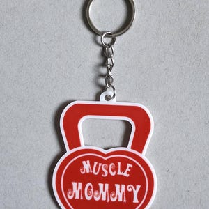 May include: Red and white keychain shaped like a kettlebell with the text "MUSCLE MOMMY" in a heart shape.