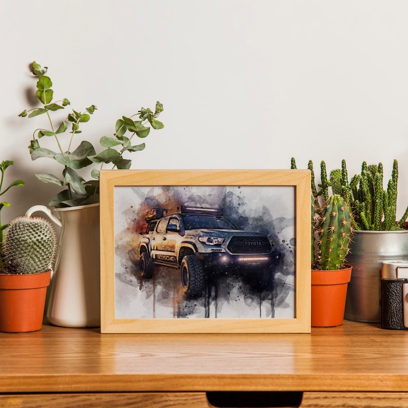 Op de afbeelding: Een ingelijst aquarel schilderij van een witte Toyota pick-up truck met een dakrek en offroad-verlichting. De truck is geplaatst tegen een wazige achtergrond in oranje en blauw.
