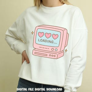 May include: White sweatshirt featuring a pink retro computer graphic with three hearts and the word "LOADING...". The design includes sparkling star accents. The text "DIGITAL FILE DIGITAL DOWNLOAD" is at the bottom.