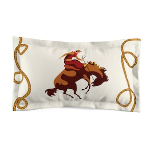 Può includere: Una federa bianca con una scena di rodeo. Presenta un cavaliere su un bronco in colori marrone e rosso. La federa ha un bordo a corda marrone dorato.