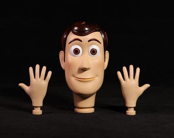 May include: A Woody action figure head and two hands, set against a black background. The head features brown hair, large eyes, and a smiling expression. The hands are open, with a beige color.