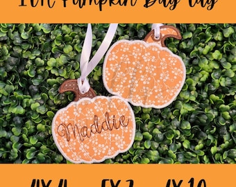 May include: Two orange pumpkin bag tags with white floral patterns and brown stems. One tag has the name "Maddie" embroidered on it. The tags are hanging with white ribbons. The text "ITH Pumpkin Bag Tag" is at the top.