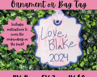 May include: A white, blue, and pink embroidered ornament or bag tag with the text "Love, Blake 2024". The ornament is on a green background.