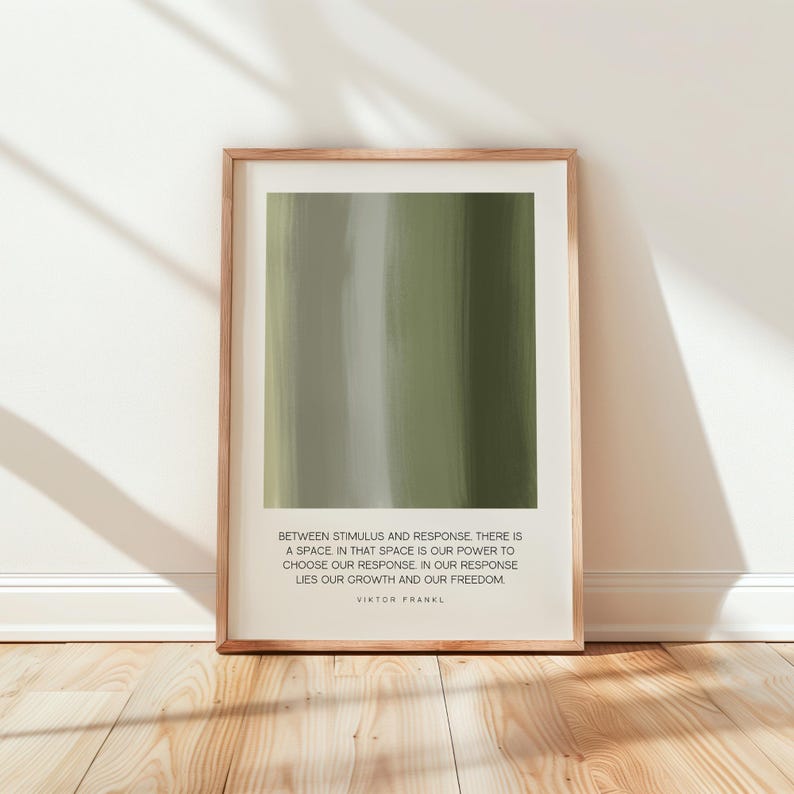 May include: A framed print featuring an abstract design of vertical brushstrokes in shades of green and gray. The print includes a quote by Viktor Frankl: "Between stimulus and response..." The frame is a light brown color.
