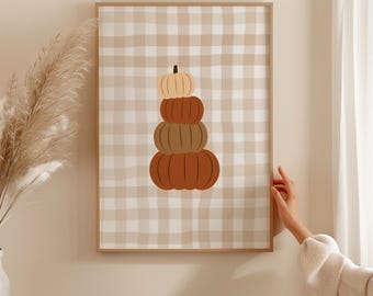May include: A framed print featuring a stack of pumpkins in shades of orange and brown. The pumpkins are arranged on a beige and white checkered background. The artwork is displayed in a wooden frame.