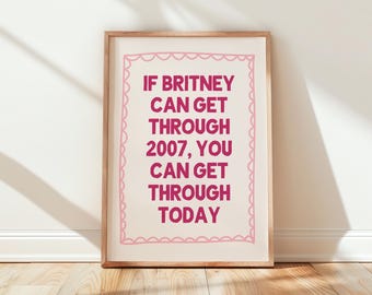 May include: A framed print with the text "IF BRITNEY CAN GET THROUGH 2007, YOU CAN GET THROUGH TODAY" in magenta. The text is centered on a cream-colored background, framed by a pink scalloped border, and set in a wooden frame.