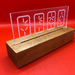 May include: A clear acrylic sign with four white etched flower designs, illuminated from behind, sits on a wooden base.