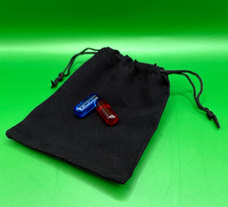 May include: A black drawstring bag with two capsule-shaped objects. One capsule is transparent blue, and the other is transparent red. The bag is made of a soft, dark fabric. The background is a solid green.