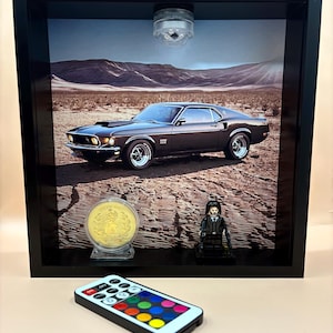 May include: A framed shadow box featuring a classic brown car image, a gold coin, and a Lego figure. A remote control with color options sits in front. The frame has a built-in light.