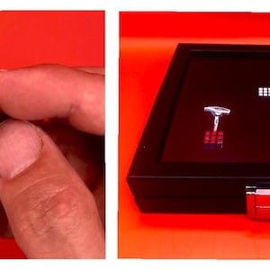 Könnte beinhalten: Ein Mini-Rubik's Cube zwischen Fingern, der seine farbigen Quadrate zeigt. Daneben befindet sich eine schwarze Vitrine mit einem Paar silberner Manschettenknöpfe mit Rubik's Cube-Design und einem kleinen Rubik's Cube-Muster.
