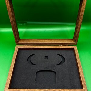 May include: Open wooden display case with a clear glass top and a black foam insert. The case has a hinged lid with a silver clasp. The interior foam has cutouts for displaying items. The wood has a natural grain.